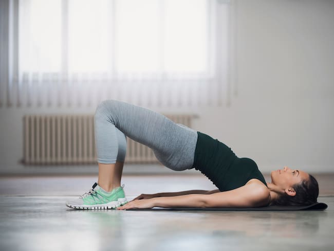 Mujer realizando ejercicio para glúteos en el suelo (Getty Images)