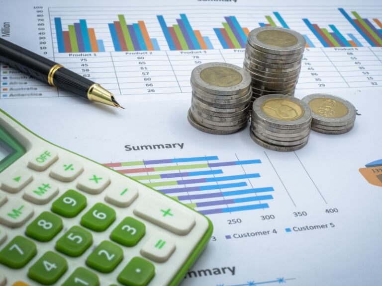 Gráficas sobre situación económica personal, con un monto de monedas sobre el papel y con una calculadora al lado (Getty Images)