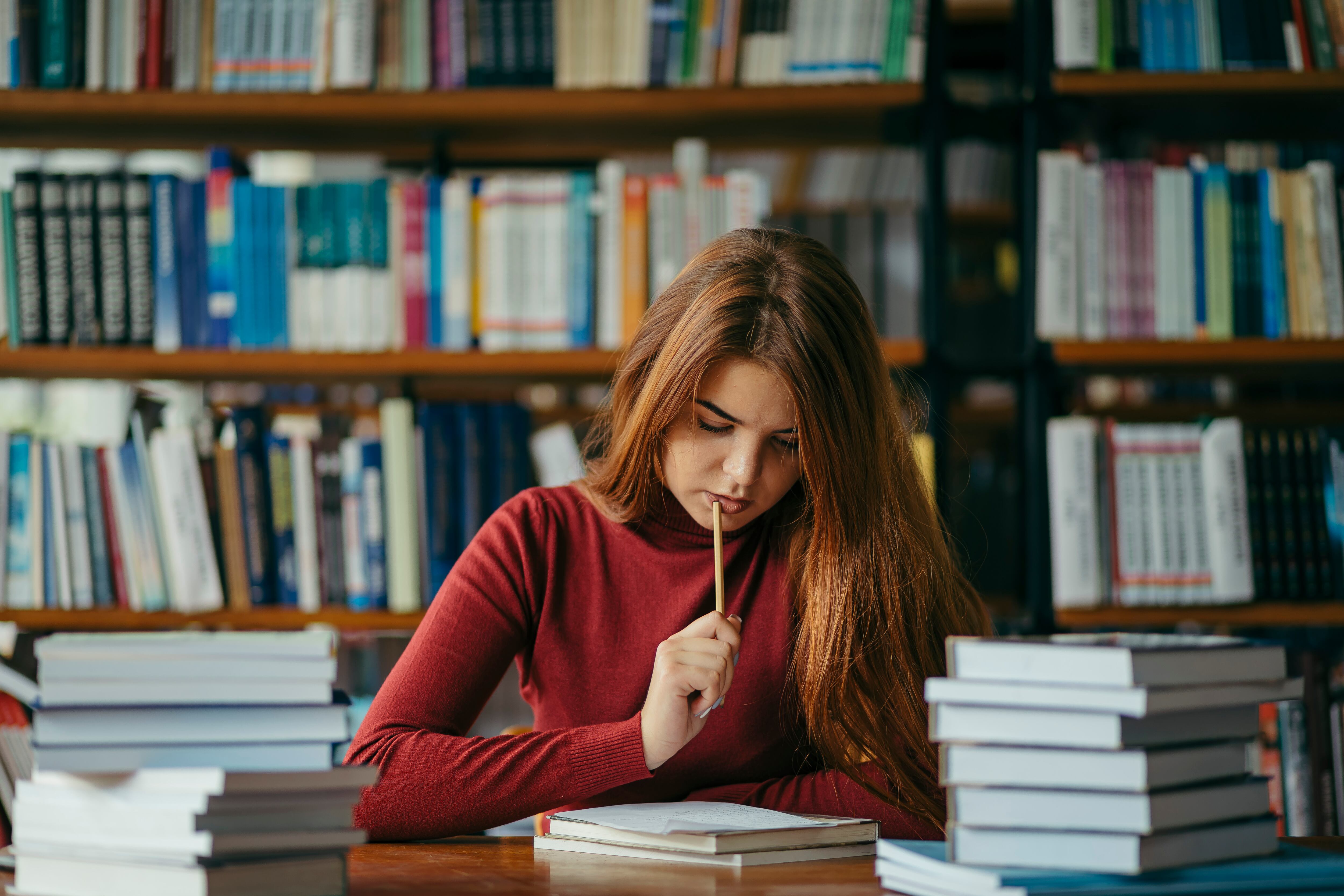 Mujer sentada en la mesa de una biblioteca leyendo unos apuntes mientras sostiene un lápiz (Getty Images)