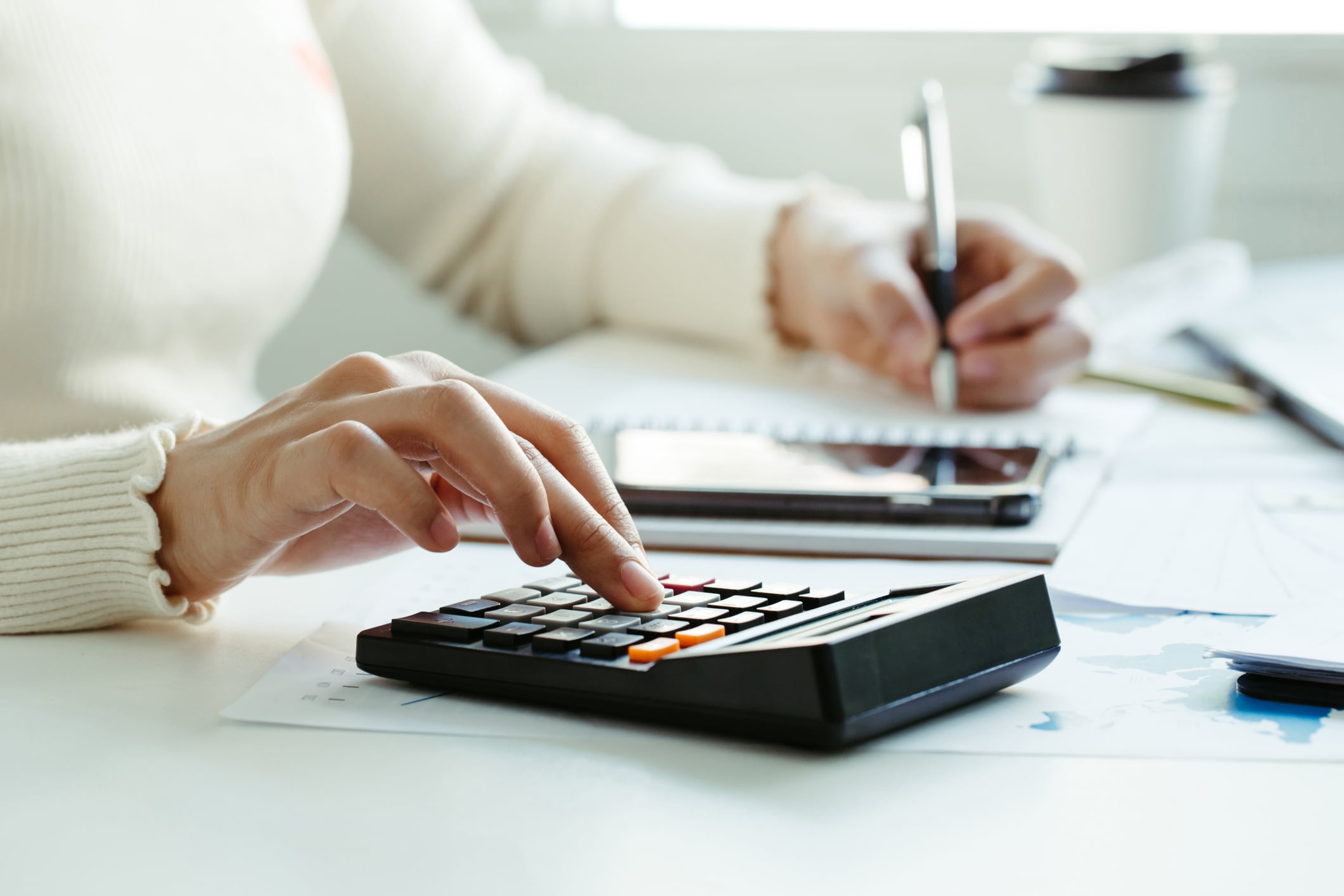 La mano de la mujer usando calculadora y escribiendo hacer nota con calcular sobre el costo en la oficina en casa (Foto vía Getty Images)