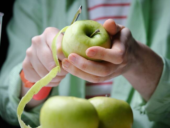 Persona pelando una manzana verde (Foto vía Getty Images)