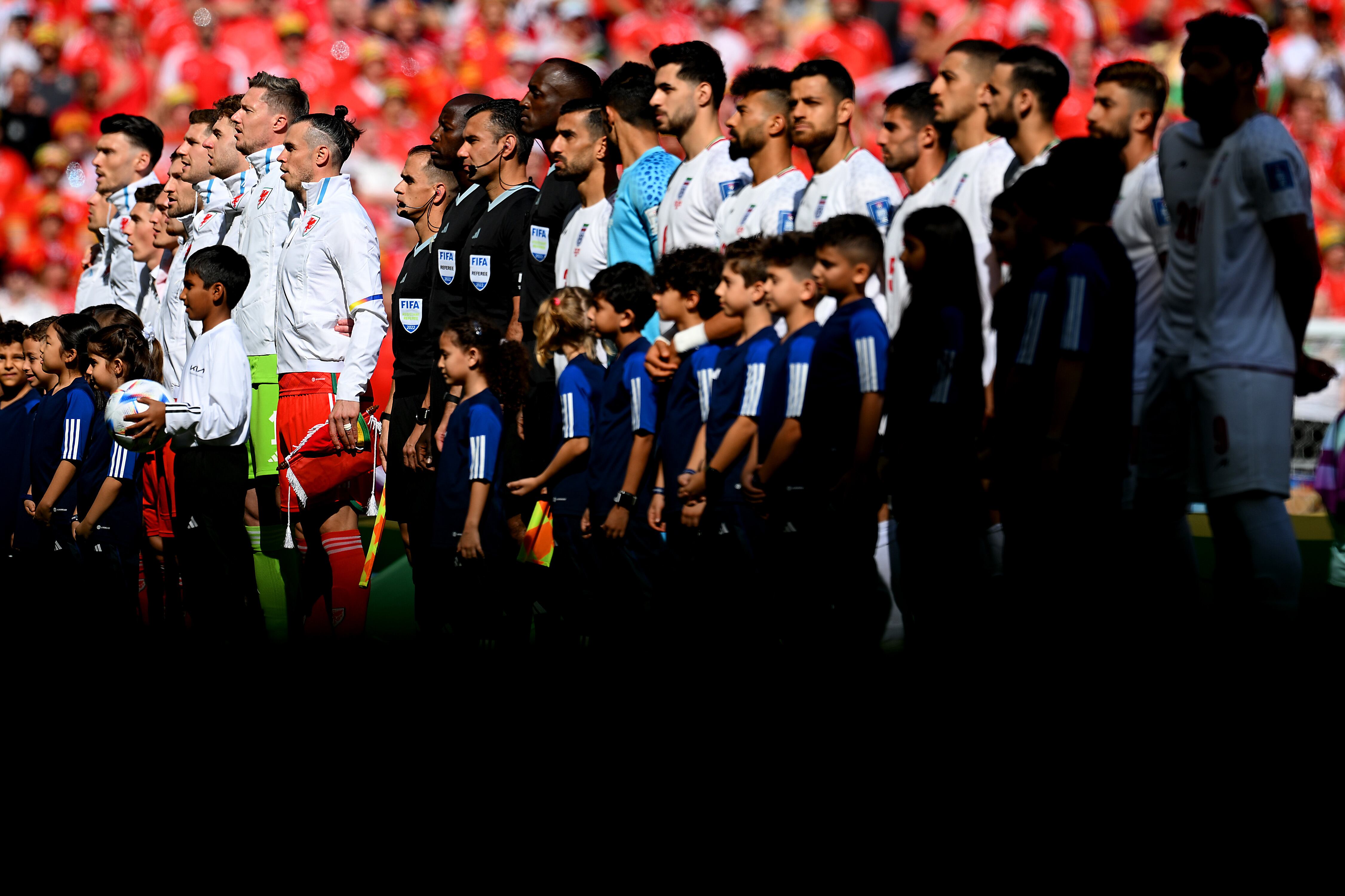 DOHA, QATAR - NOVEMBER 25: Players and match officials line up prior to the FIFA World Cup Qatar 2022 Group B match between Wales and IR Iran at Ahmad Bin Ali Stadium on November 25, 2022 in Doha, Qatar. (Photo by Matthias Hangst/Getty Images)