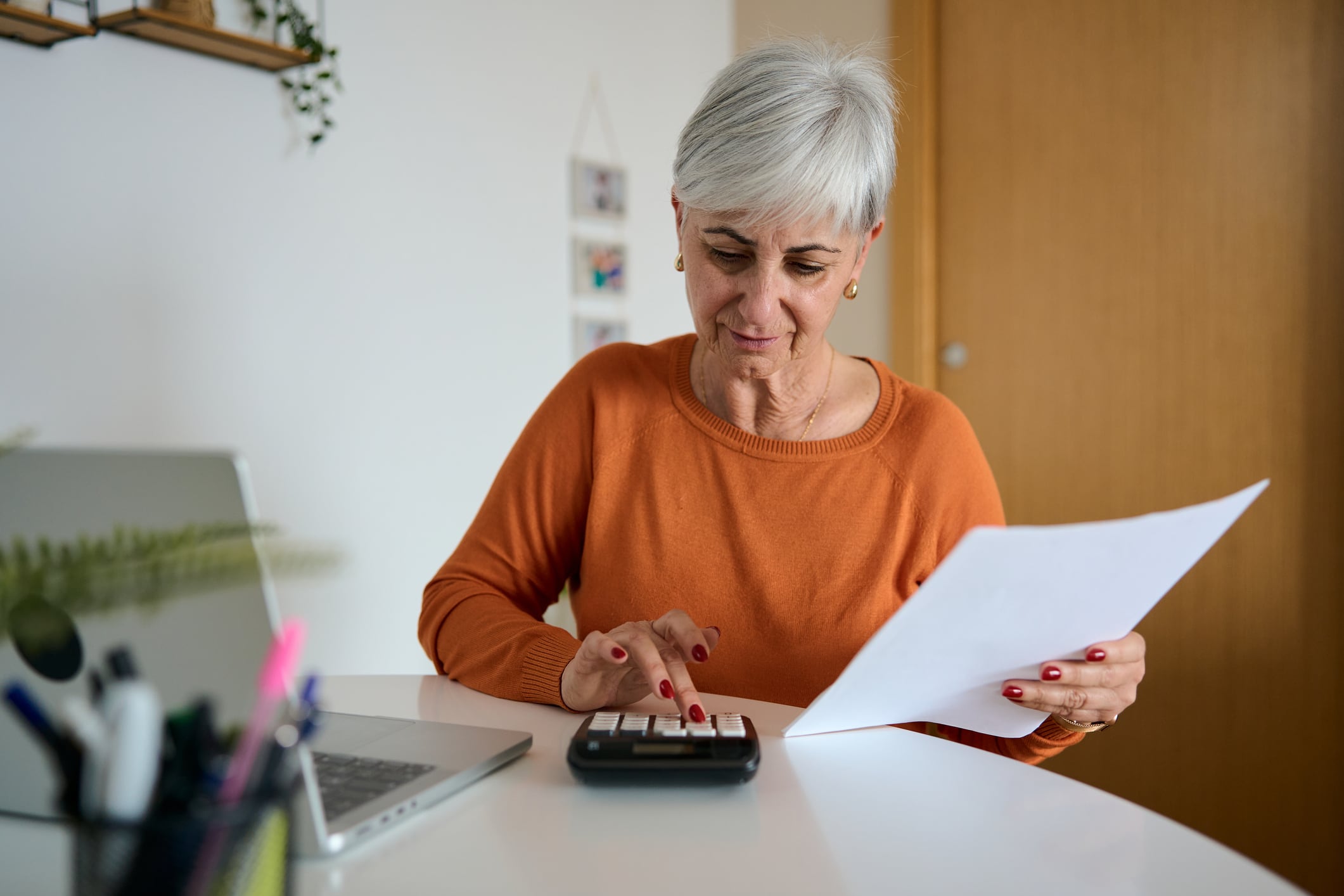 Mature woman working on finances at home, reviewing documents and using a calculator for budgeting and planning