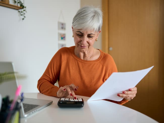 Mature woman working on finances at home, reviewing documents and using a calculator for budgeting and planning