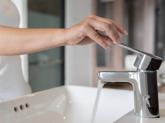 Mujer abriendo el grifo de agua del lavamanos (Foto vía GettyImages)
