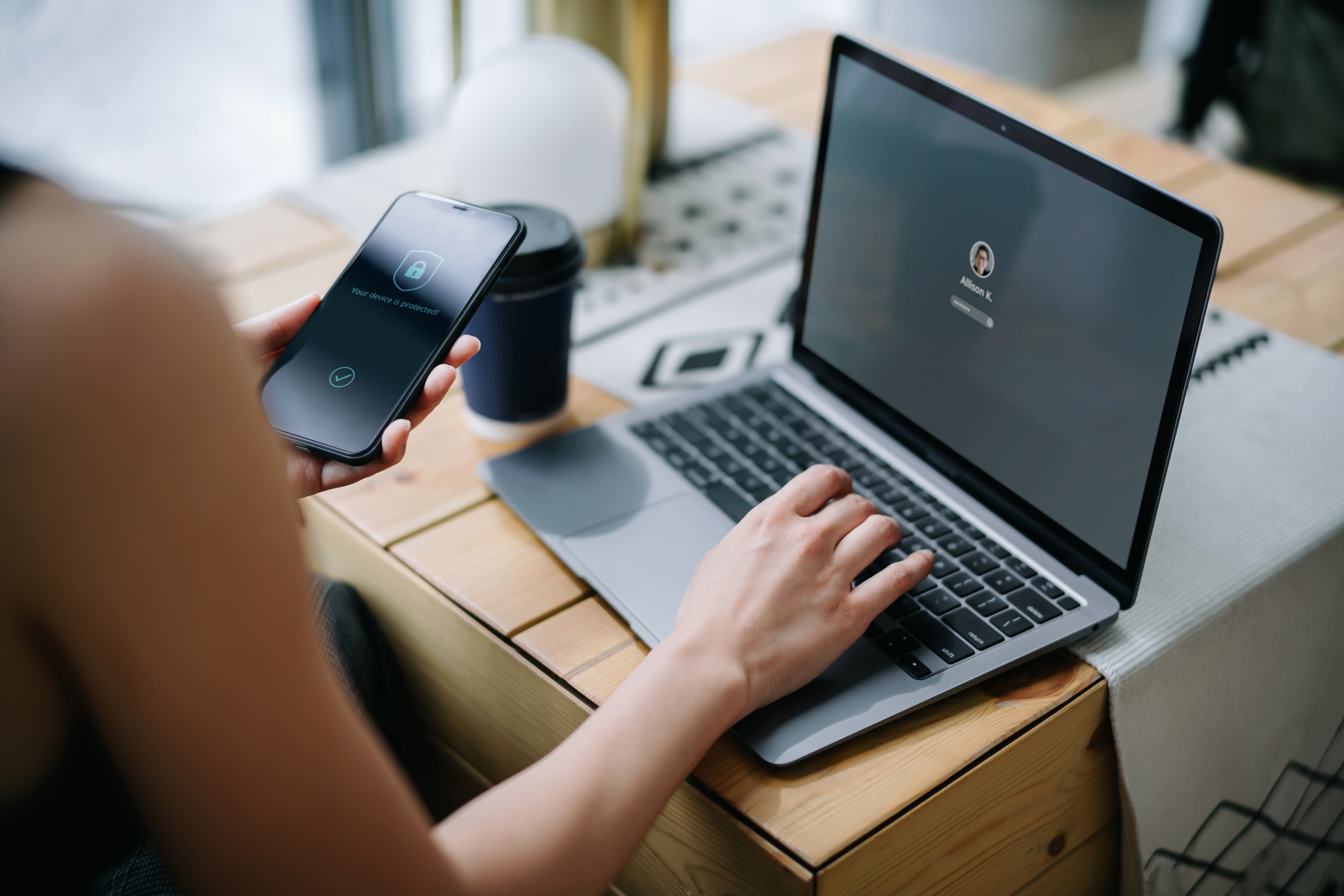 Young businesswoman working on desk, logging in to her laptop and holding smartphone on hand with a security key lock icon on the screen. Privacy protection, internet and mobile security concept