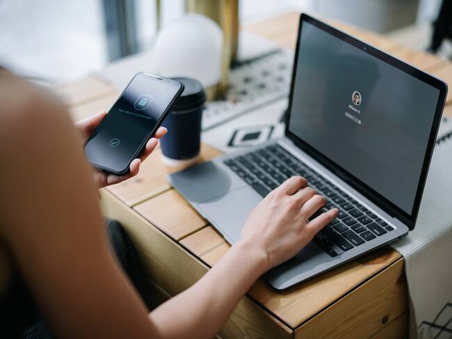 Young businesswoman working on desk, logging in to her laptop and holding smartphone on hand with a security key lock icon on the screen. Privacy protection, internet and mobile security concept