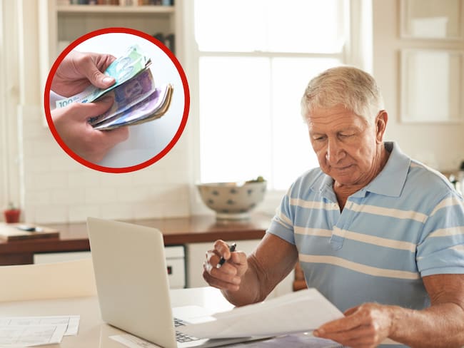Hombre con una computadora y papeles sobre una mesa junto a unos billetes (Foto vía Getty Images)