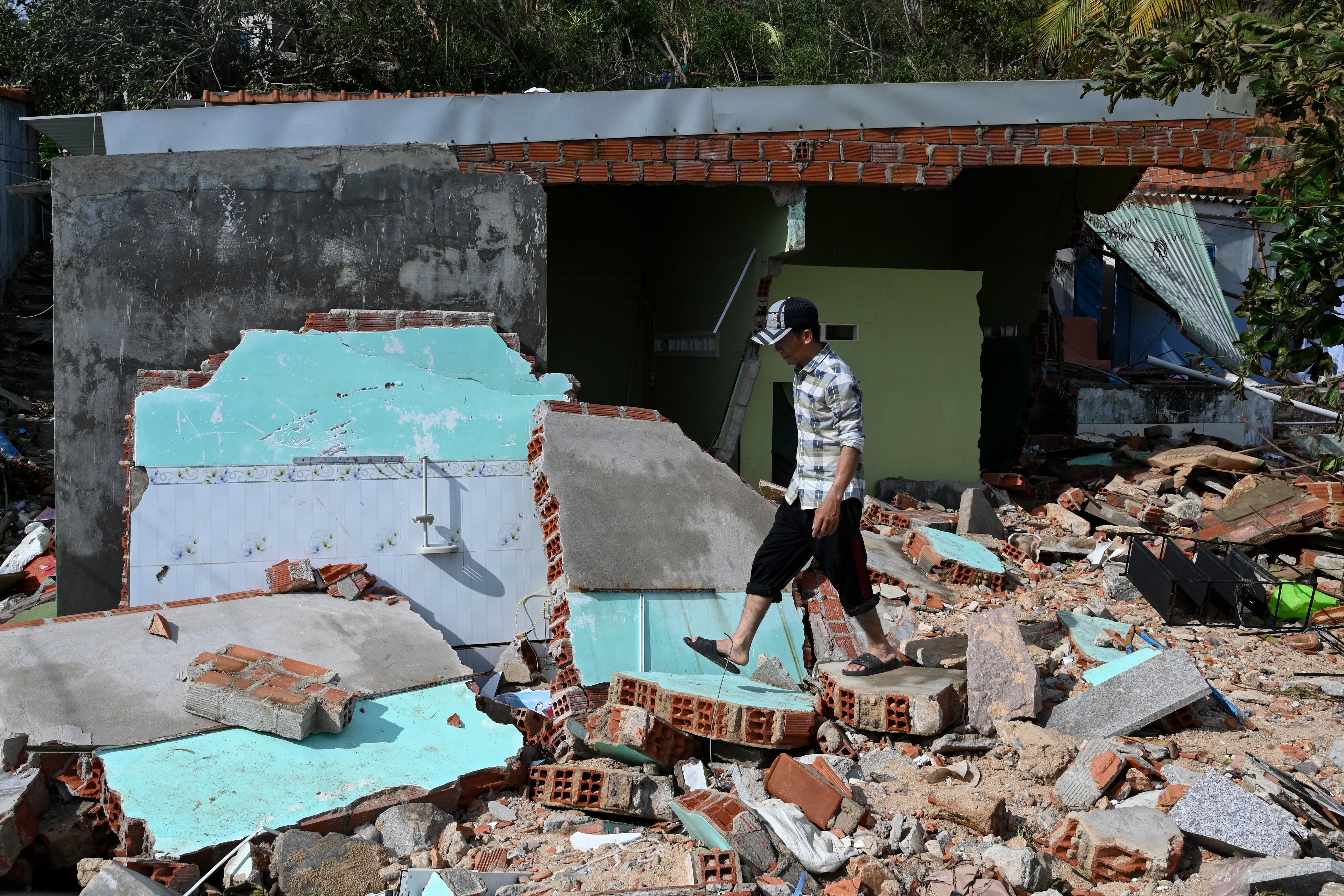 A resident walks over the debris of a structure destroyed in high winds in Nhon Hai fishing village near Quy Nhon in the aftermath of Typhoon Kalmaegi in Gia Lai province, central Vietnam on November 7, 2025. Typhoon Kalmaegi churned across Vietnam on November 7, claiming five more lives after its devastating passage through the Philippines where the death toll rose to 188. (Photo by NHAC NGUYEN / AFP)