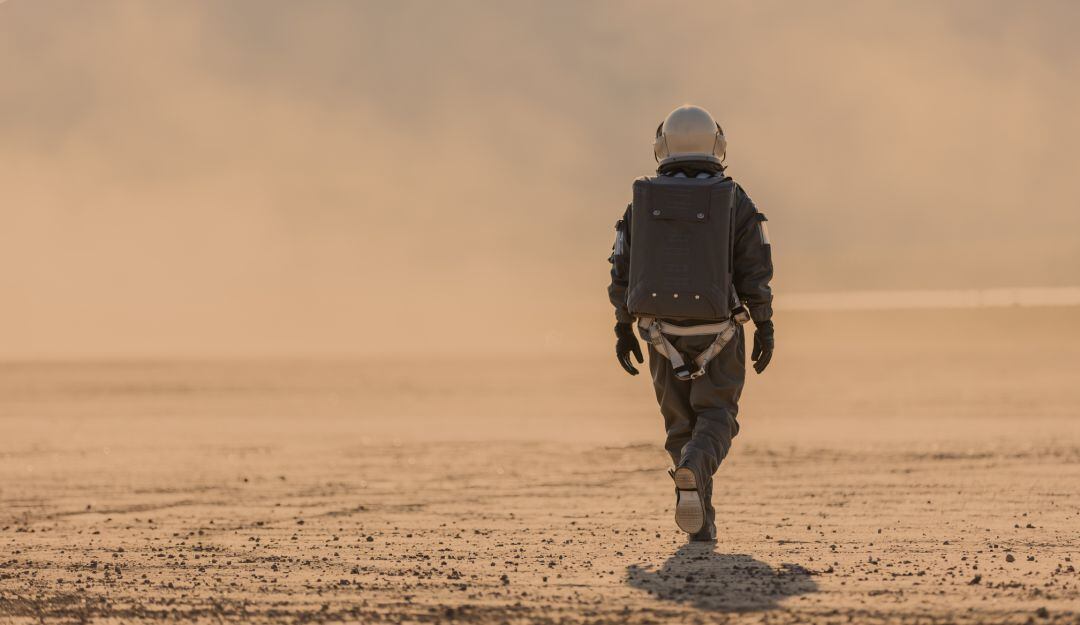 Foto de un astronauta con traje espacial y casco en Marte alejándose de la cámara hacia una tormenta de polvo a lo lejos