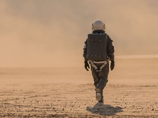 Foto de un astronauta con traje espacial y casco en Marte alejándose de la cámara hacia una tormenta de polvo a lo lejos