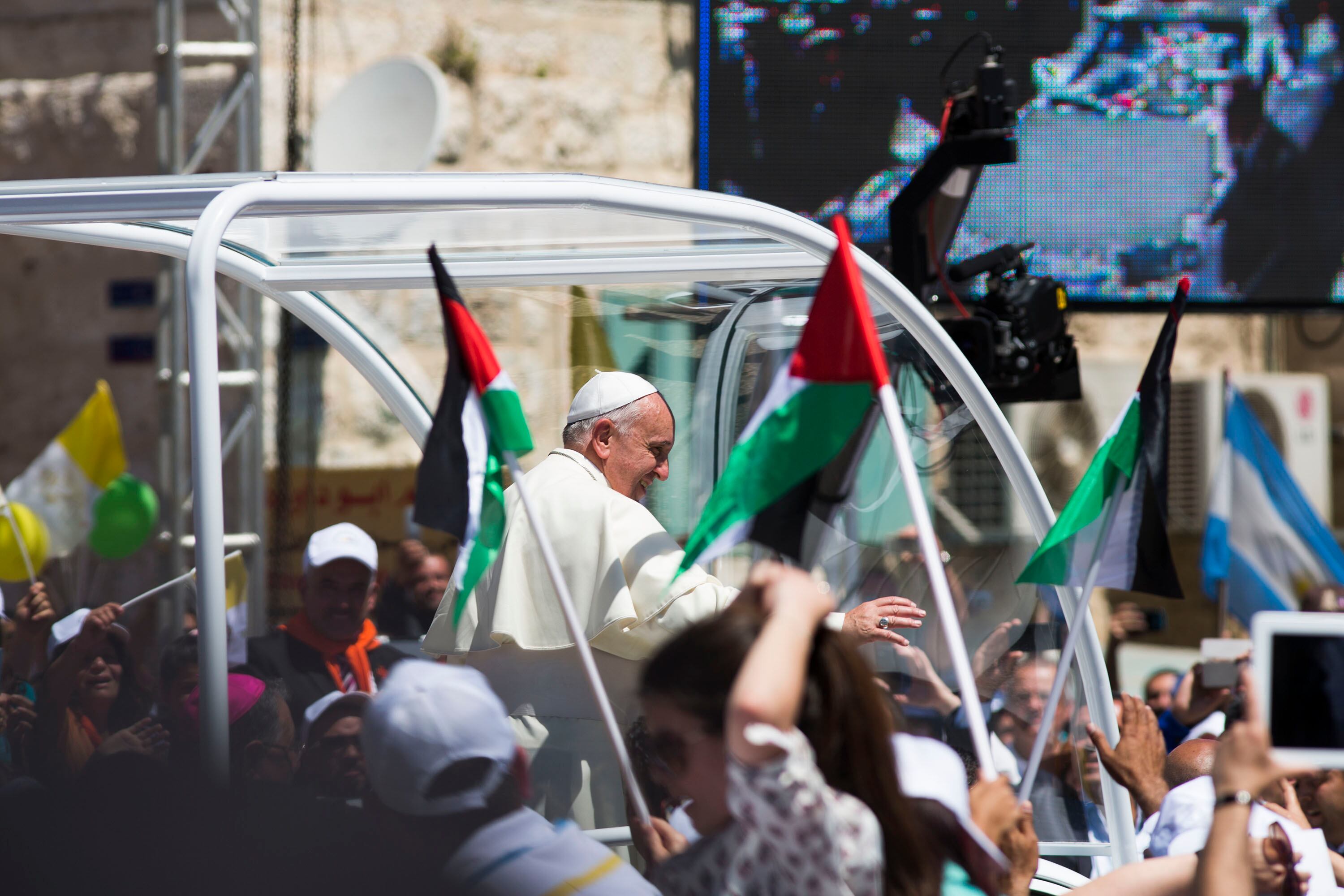 BETHLEHEM, WEST BANK - MAY 25:   Pope Francis arrives in Manger Square to take part in a Mass held at the Church of Nativity as crowds watch and wave flags in the foreground on May 25, 2014, in Bethlehem, West Bank.  Pope Francis addressed the Israeli-Palestinian conflict as "unacceptable" and urged both sides to find courage in seeking a peaceful solution.  (Photo by Ilia Yefimovich/Getty Images)