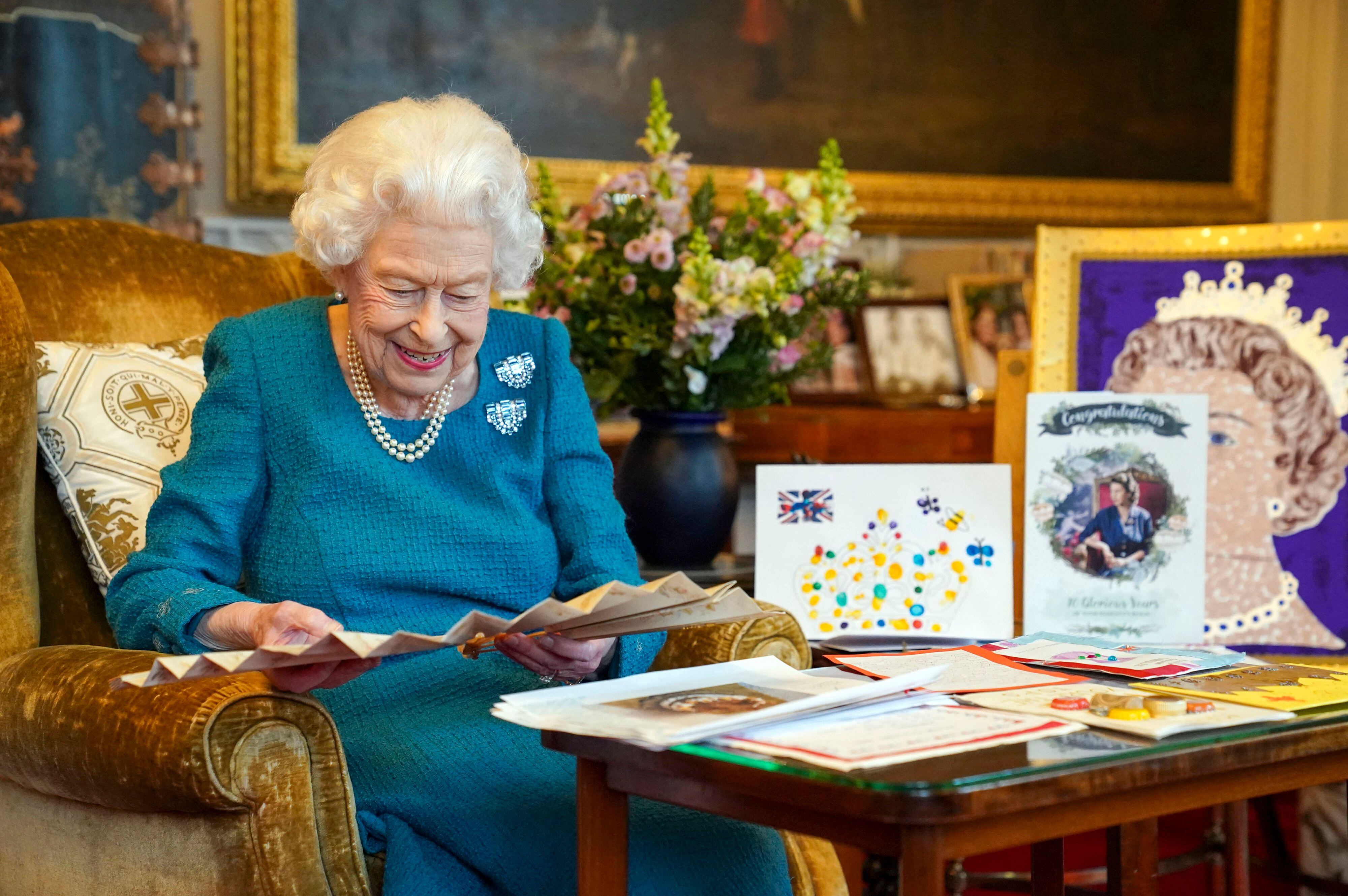 TOPSHOT - A picture released in London on February 4, 2022, and taken last month, shows Britain's Queen Elizabeth II looking at Queen Victoria's Autograph fan, alongside a display of memorabilia from her Golden and Platinum Jubilees, in the Oak Room at Windsor Castle, west of London. - Queen Elizabeth II on February 6, 2022, becomes the first British monarch to reign for 70 years, heralding the start of her Platinum Jubilee year despite her retreat from public view. But the landmark date this weekend will see little fanfare, as the 95-year-old monarch traditionally spends the anniversary of the death of her father in private. (Photo by Steve Parsons / POOL / AFP) (Photo by STEVE PARSONS/POOL/AFP via Getty Images)