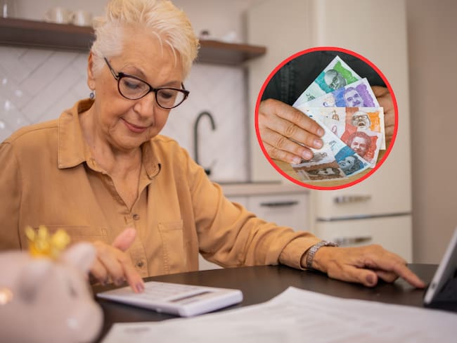 Mujer adulta mayor haciendo cuentas en una calculadora y de fondo dinero colombiano (Foto vía Getty Images)