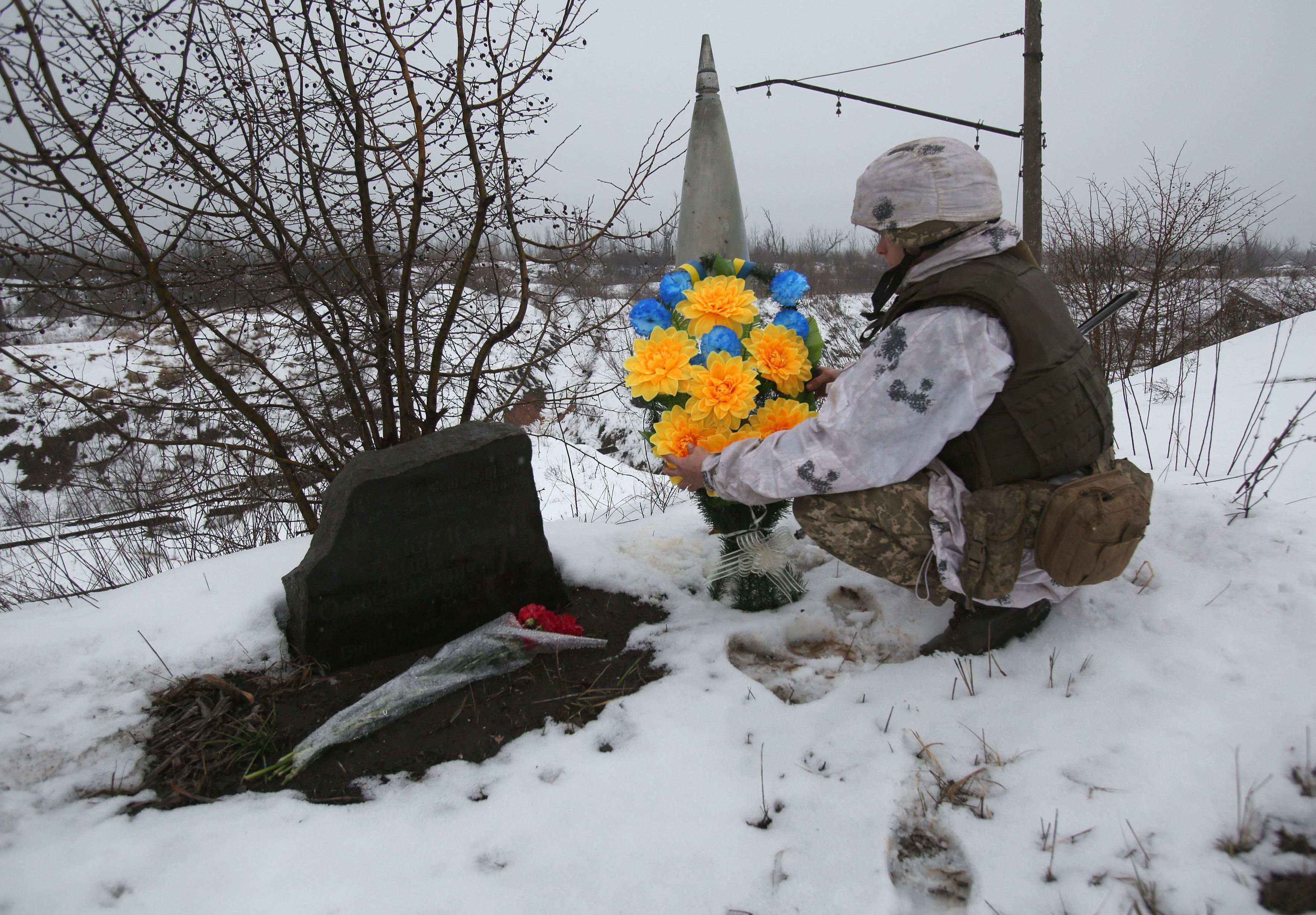 TOPSHOT - An Ukrainian servicemen lays flowers with the Ukrainian flag colors to the place where one of his friend was killed in 2017 on the frontline with the Russia-backed separatists near Avdiivka, Donetsk region, on February 2, 2022. (Photo by Anatolii STEPANOV / AFP) (Photo by ANATOLII STEPANOV/AFP via Getty Images)