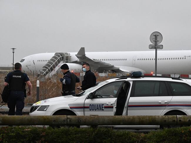French customs officers stand next to a customs car with an Airbus A340 in the background which was grounded on the tarmac since December 21 over suspected "human trafficking", at the Vatry airport, north-eastern France on December 25, 2023. Two Indians passengers on the flight grounded since December 21, in the Marne region of France on suspicion of human trafficking will be presented to an examining magistrate on December 25, with possible indictment, while most of the other passengers are due to take off for India later on December 25. (Photo by FRANCOIS NASCIMBENI / AFP) (Photo by FRANCOIS NASCIMBENI/AFP via Getty Images)