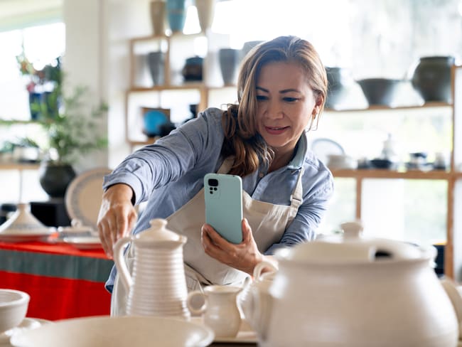 Mujer empresaria tomando fotos de sus productos en una tienda de cerámica para redes sociales (Getty Images)