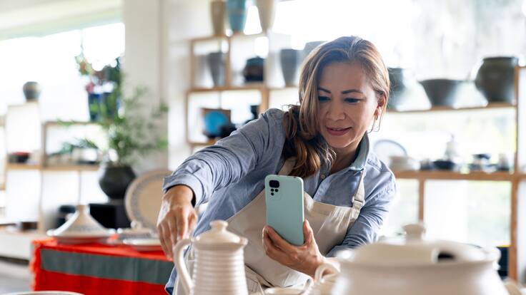 Mujer empresaria tomando fotos de sus productos en una tienda de cerámica para redes sociales (Getty Images)