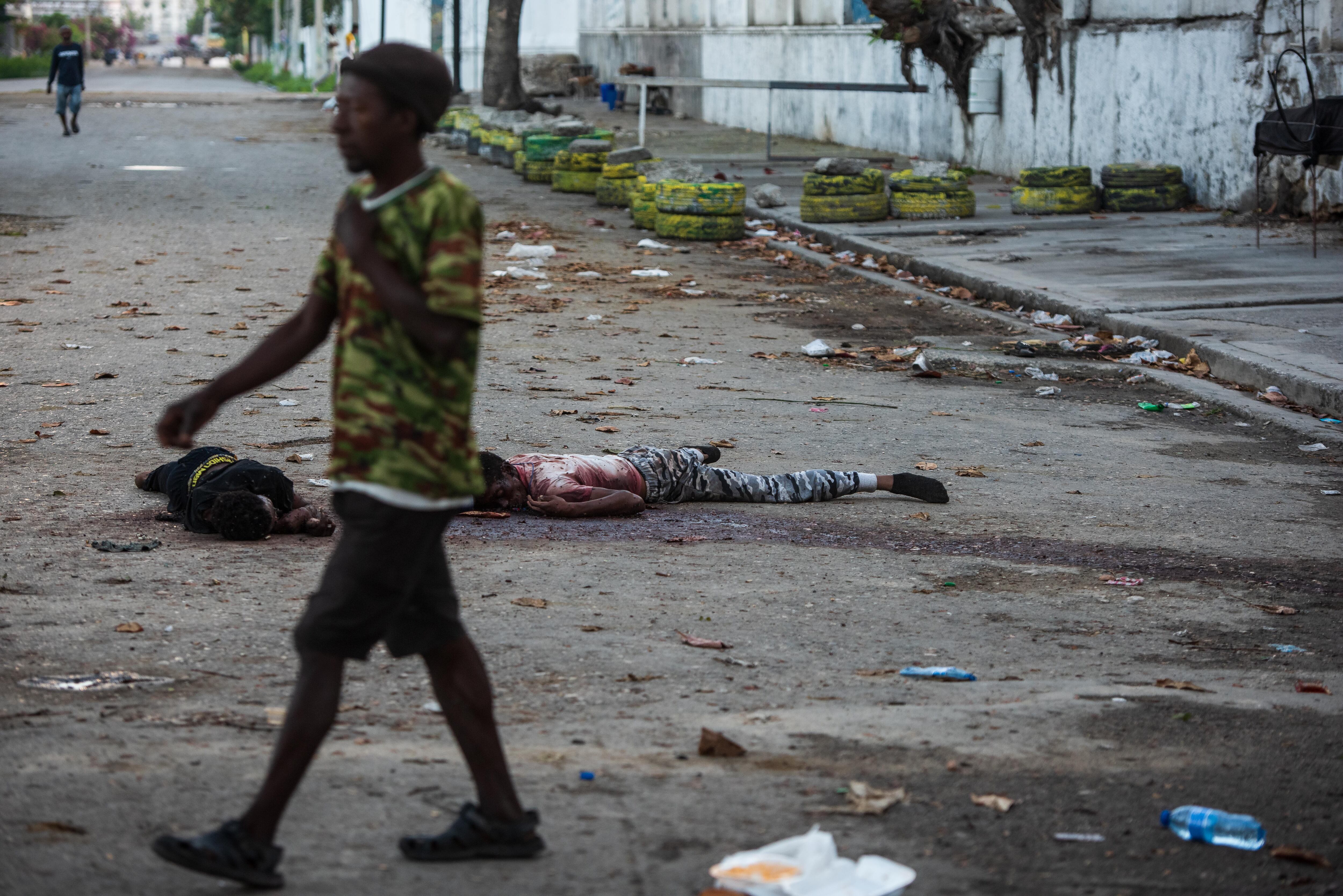 Un hombre pasa frente uno cadáveres este domingo, en una calle de Puerto Príncipe (Haití). Al menos una decena de personas murió tras el ataque anoche a la prisión civil de Puerto Príncipe por parte de bandas armadas, que habrían liberado a numerosos delincuentes importantes durante su asalto al presidio. 
Foto: EFE/ Johnson Sabin