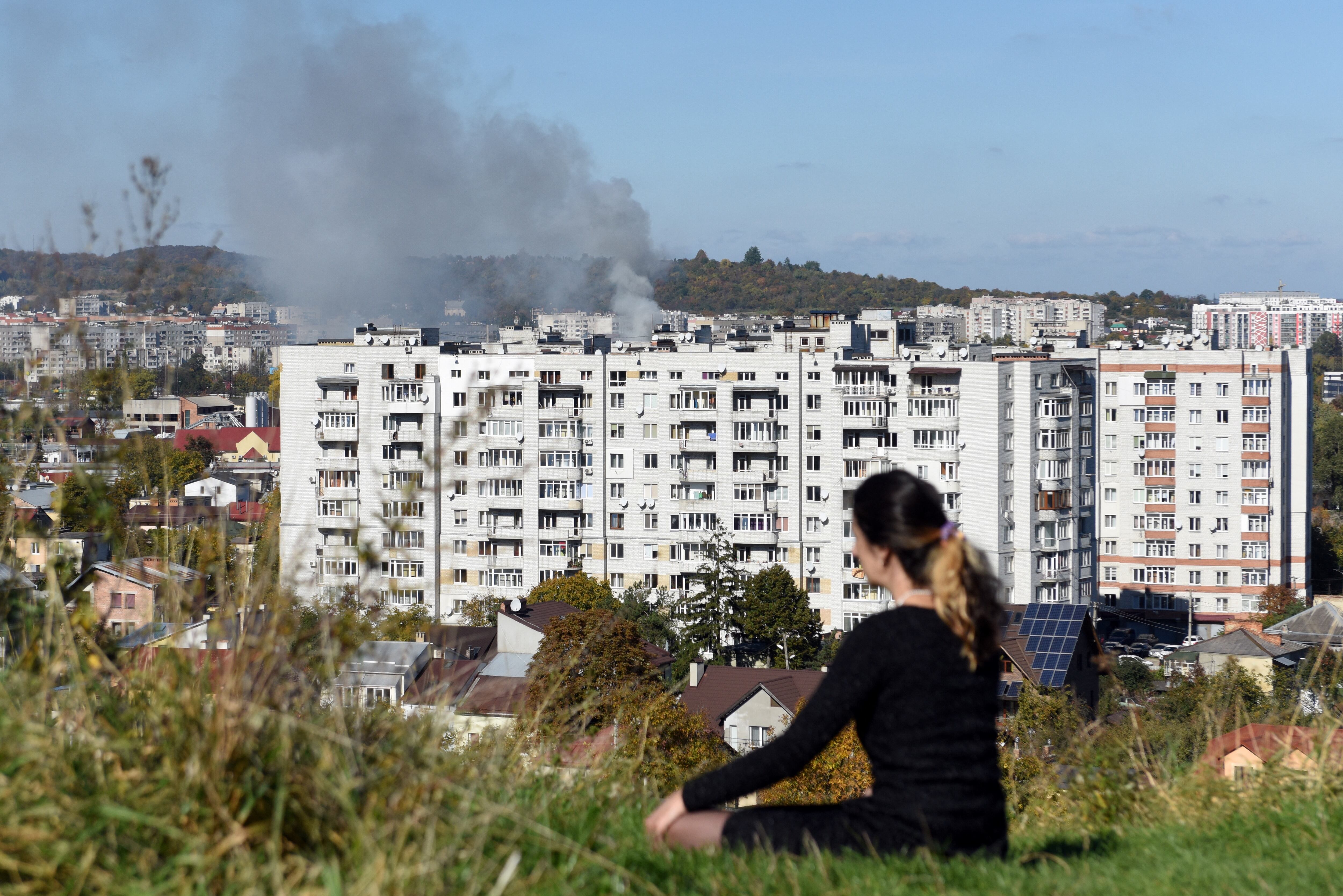 Una mujer se sienta en la colina mientras el humo se eleva sobre los edificios en la ciudad de Lviv, en el oeste de Ucrania, después de un ataque con misiles rusos / AFP