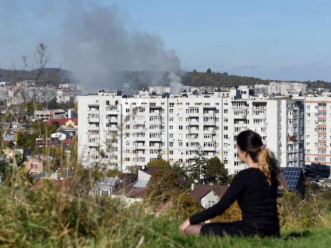 Una mujer se sienta en la colina mientras el humo se eleva sobre los edificios en la ciudad de Lviv, en el oeste de Ucrania, después de un ataque con misiles rusos / AFP