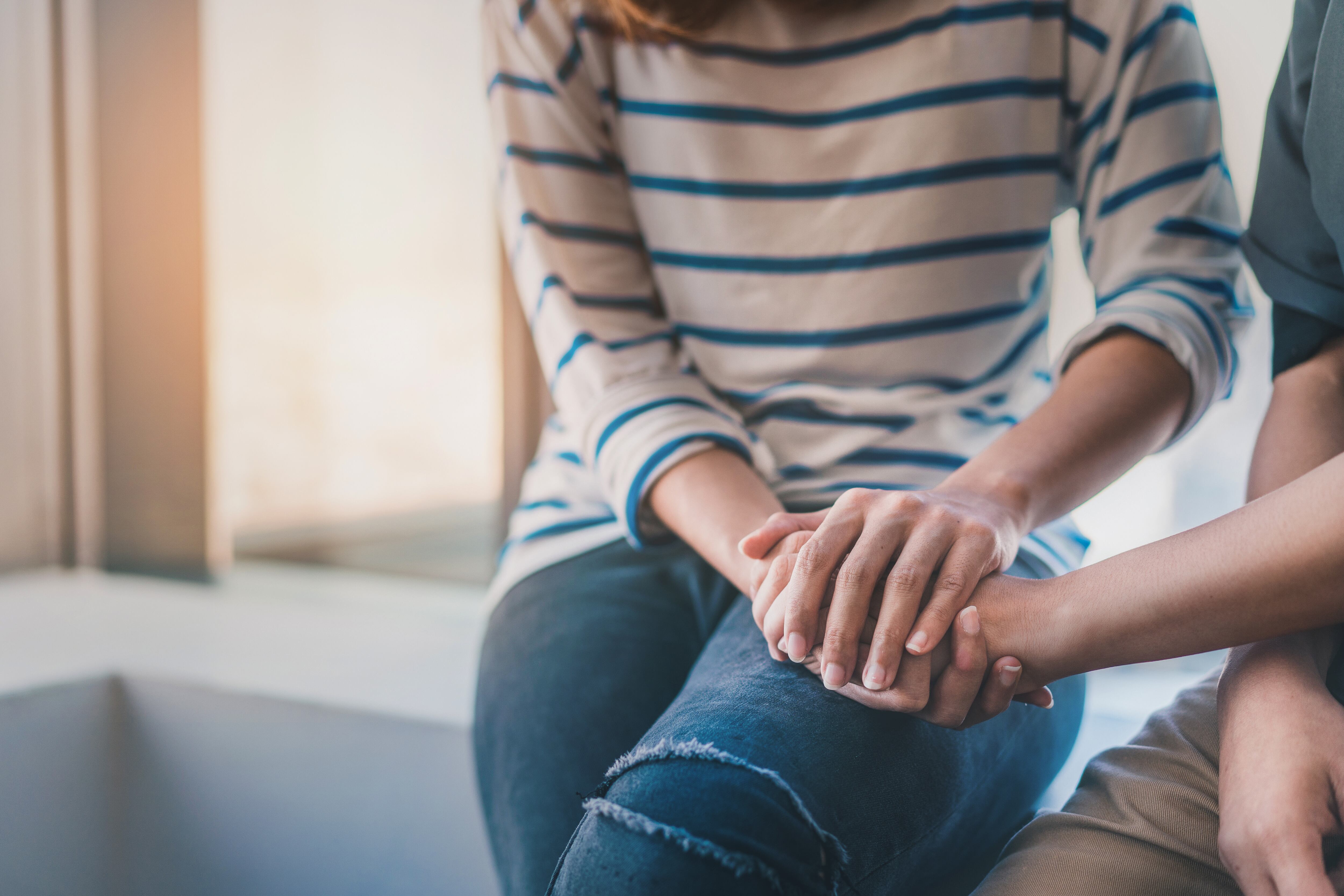 Young woman sitting and touch young depressed asian woman for encouragement near window, Selective focus, PTSD Mental health concept.
