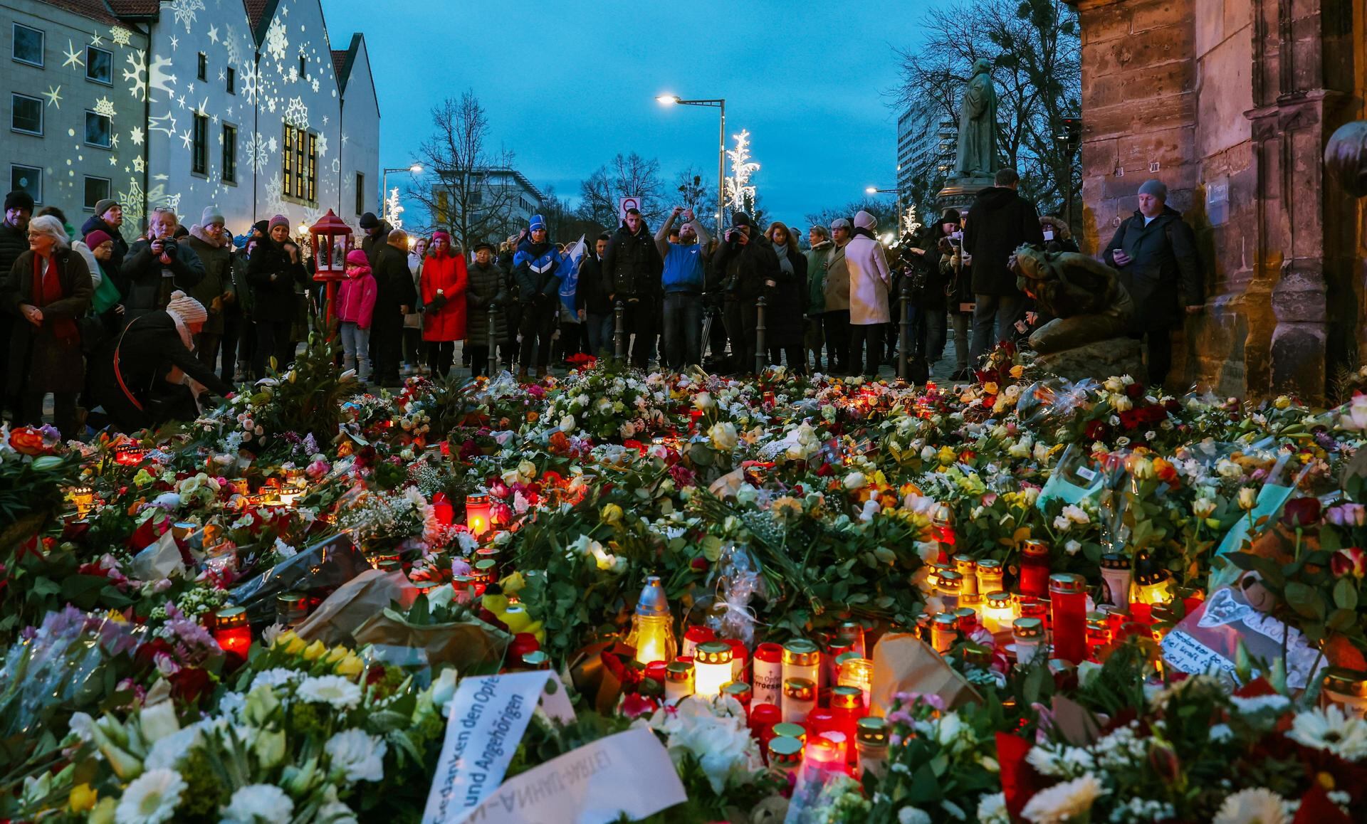 MAGDEBURGO (ALEMANIA), 21/12/2024.- Varias personas junto a flores y velas depositadas en honor a la victimas a las cinco personas fallecidas ayer en un atropello, este sábado en Magdeburgo.Horst Nopens