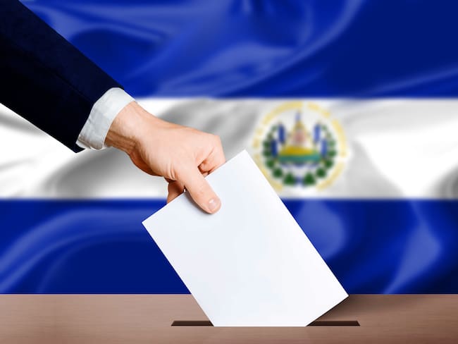 El Salvador presidential elections concept. Hand holding ballot in voting ballot box with El Salvador flag in background