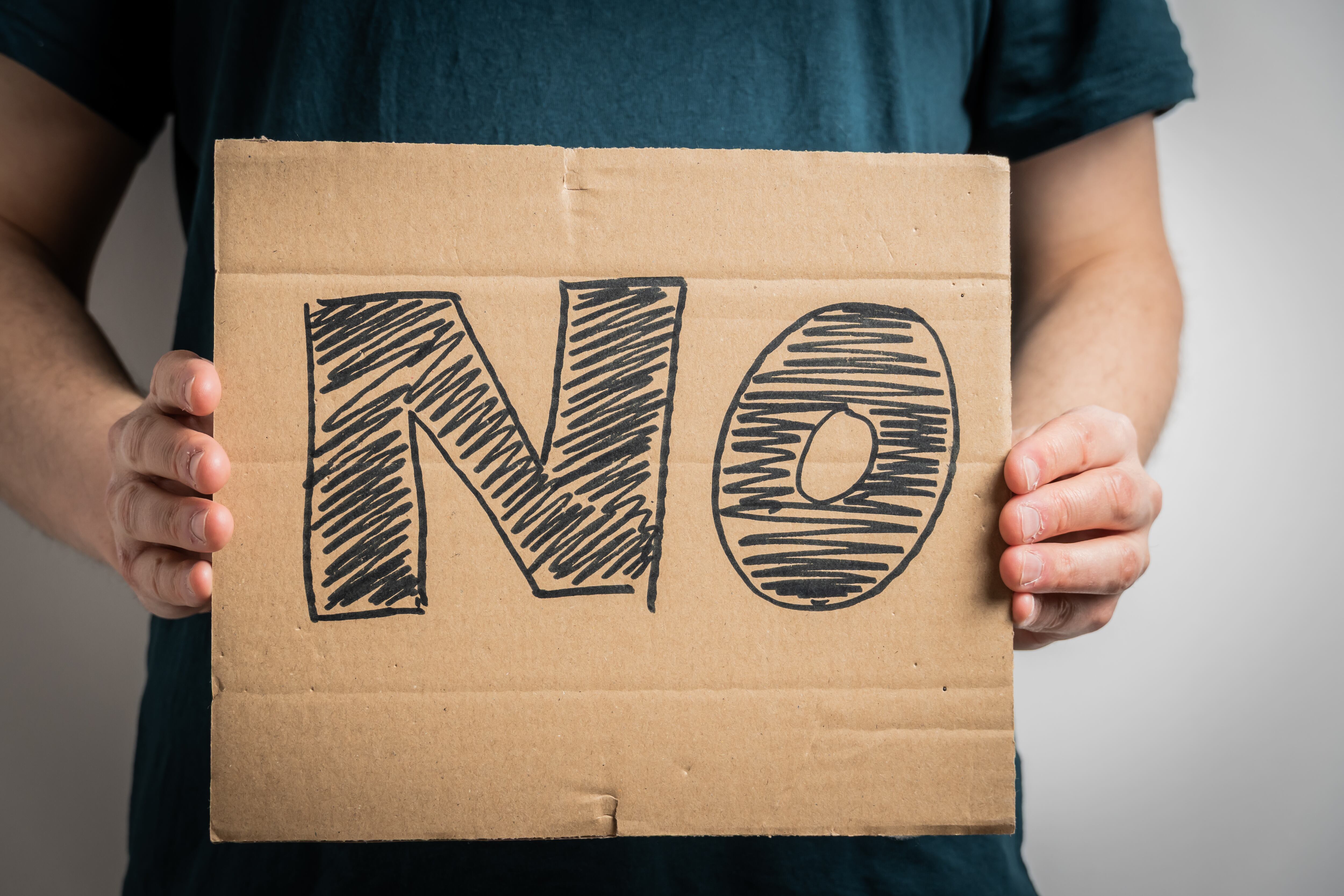 Anonymous protester showing sign with word NO, symbolizing rejection, disagreement, or resistance