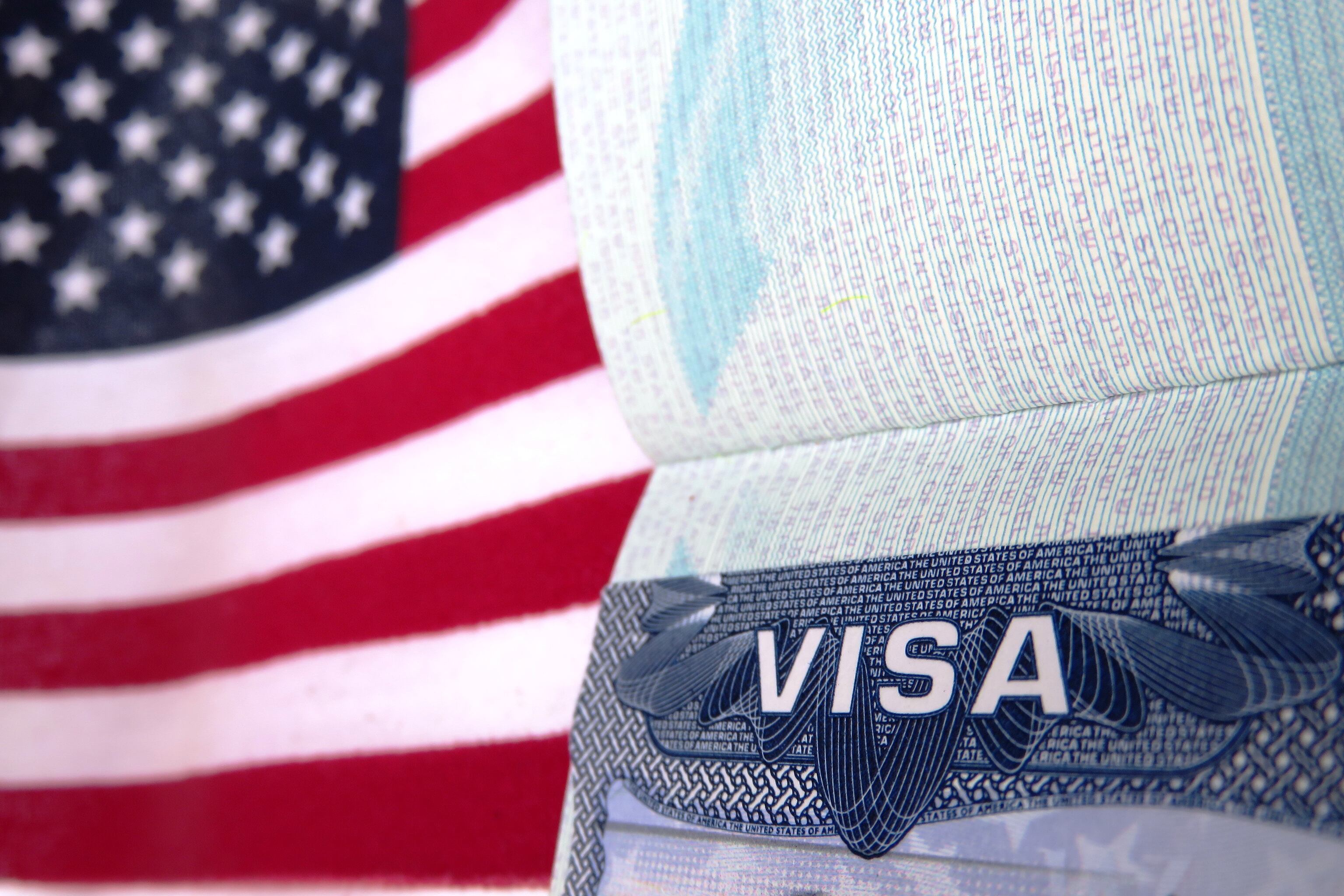 Bandera de Estados Unidos al fondo y encima la visa americana abierta / Foto: GettyImages