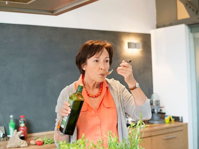 Mujer en la cocina comiendo una cucharada de aceite de oliva (Foto vía Getty Images)