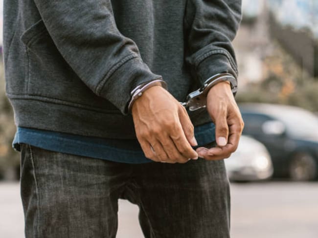 Under arrest, a man's hands with clenched fists are handcuffed behind him. Black background with copy space.