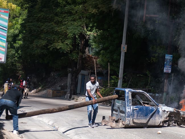 AME9132. PUERTO PRÍNCIPE (HAITÍ), 19/11/2024.- Personas sostienen un tronco en una vía este martes, en una calle de Puerto Príncipe (Haití).