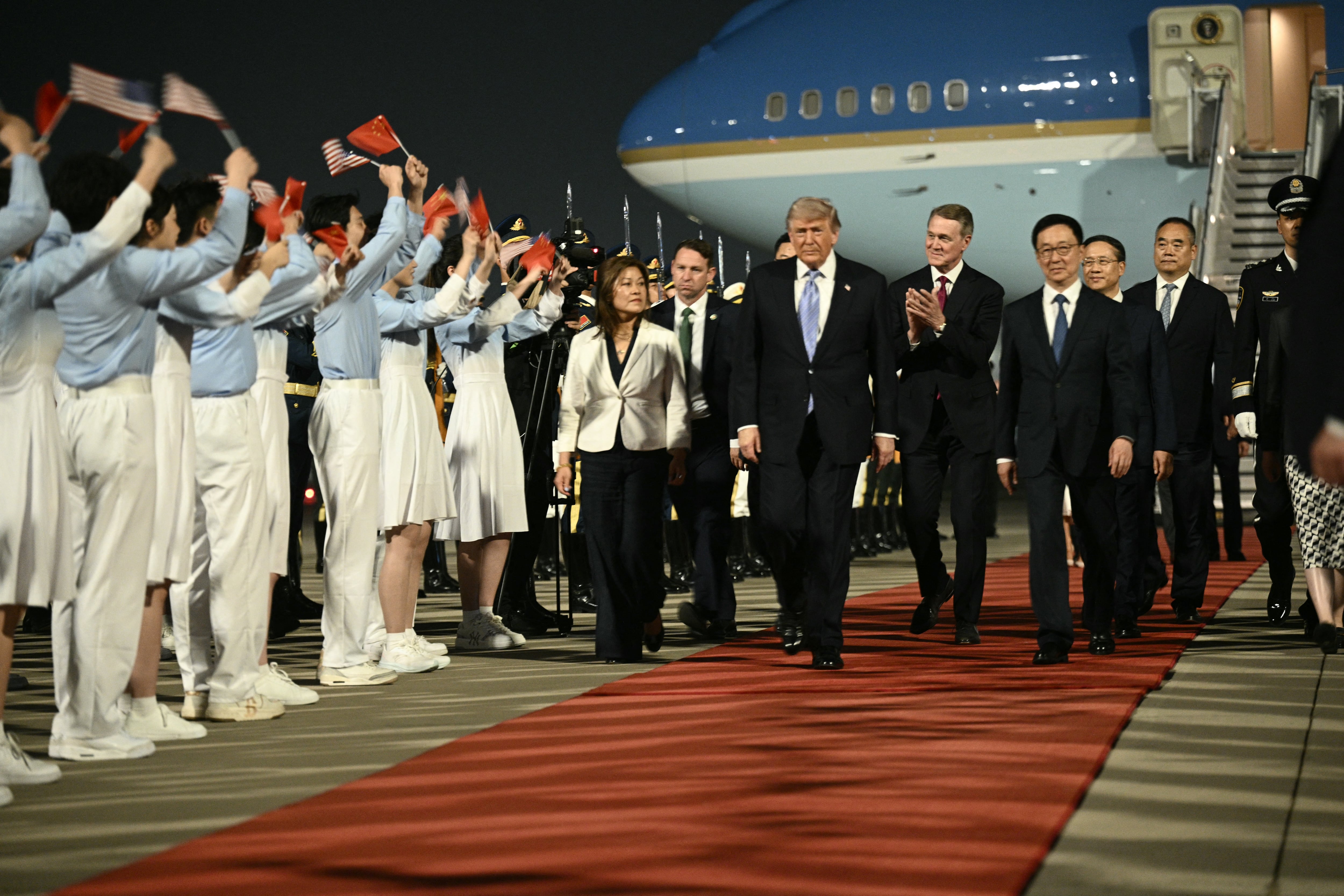 US President Donald Trump (C), US Ambassador To china David Perdue (center-R) escorted by China's Vice President Han Zheng (R) are greeted by Chinese youth upon arriving at Beijing Capital Airport in Beijing on May 13, 2026. (Photo by Brendan SMIALOWSKI / AFP)