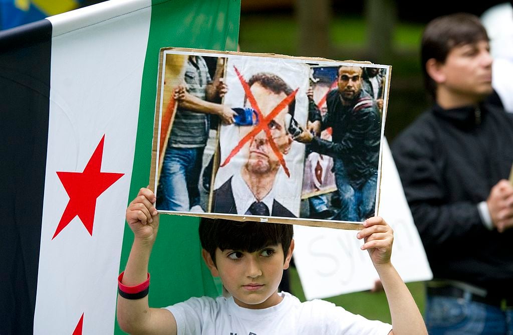 A boy holds a placard with a crossed-over image of Syrian President Bashar al-Assad on August 8, 2012 outside the Russian embassy in Stockholm, during a demonstration by hundreds of protesters against Russian support for al-Assad. AFP PHOTO / SCANPIX SWEDEN / FREDRIK SANDBERG **  SWEDEN OUT  **        (Photo credit should read FREDRIK SANDBERG/AFP/GettyImages)