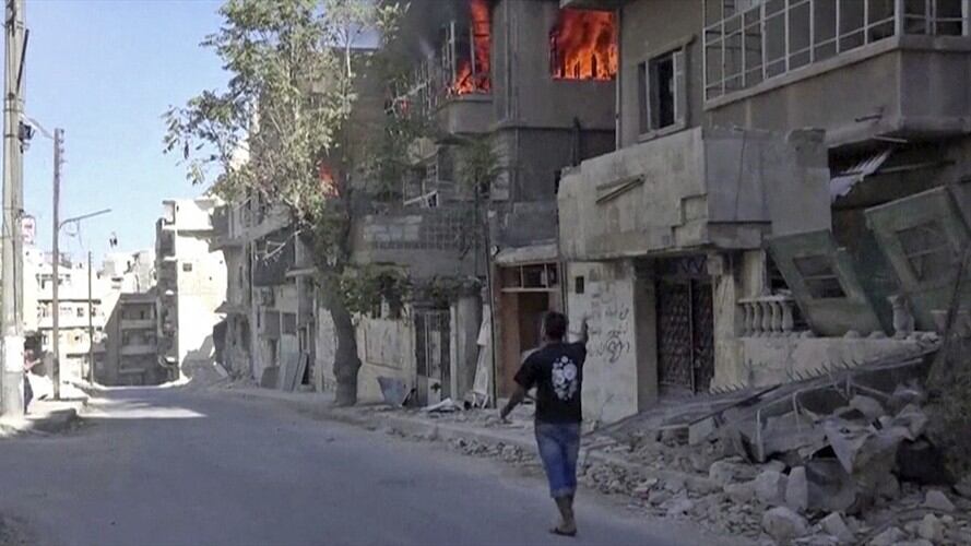 Hombre pasando por una casa en llamas en Alepo, Siria.  Foto: Associated Press - AP.