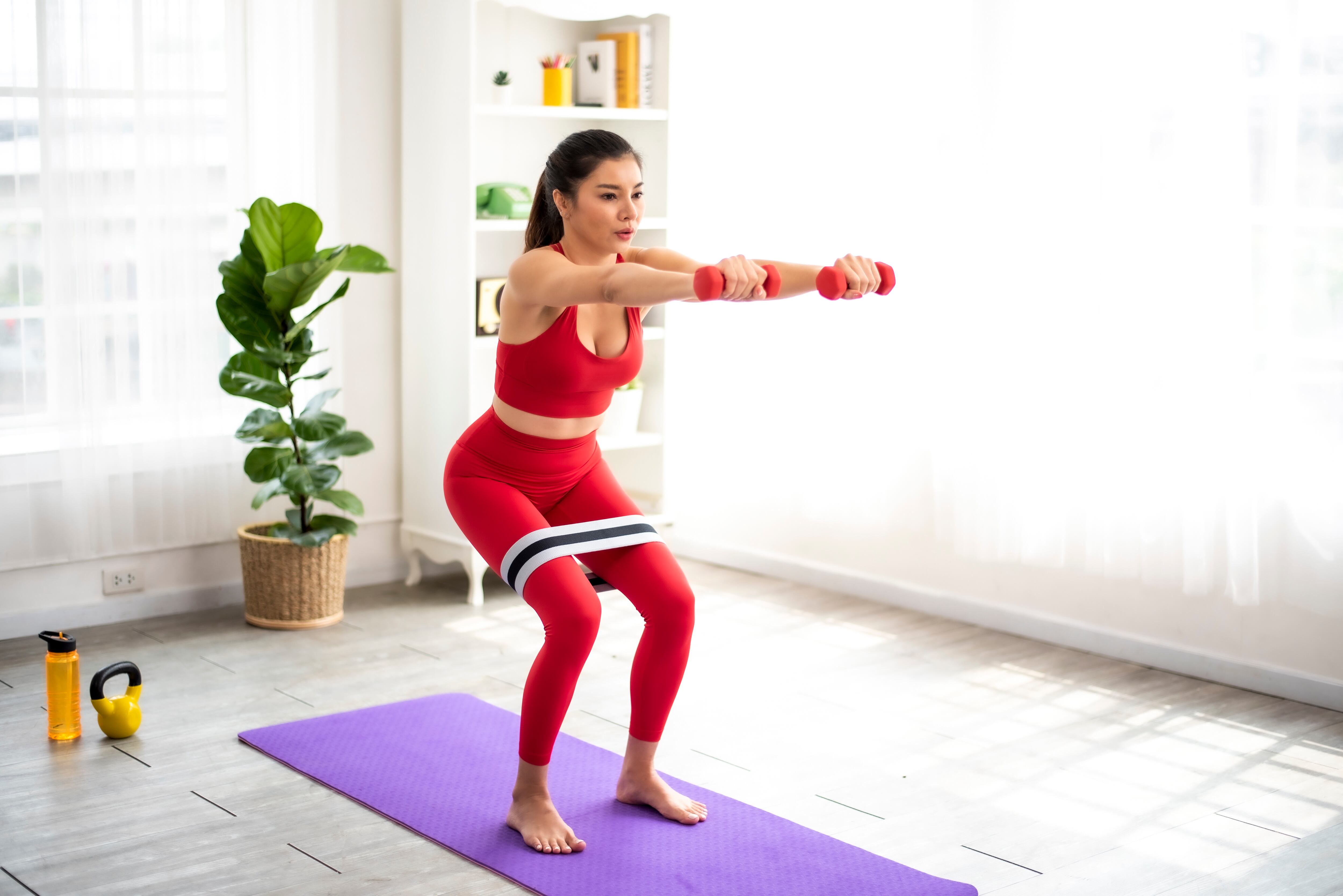 Mujer haciendo ejercicio en casa con unas pesas y una banda elástica (Foto vía Getty Images)