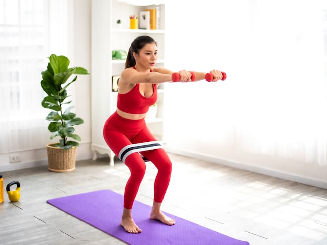 Mujer haciendo ejercicio en casa con unas pesas y una banda elástica (Foto vía Getty Images)