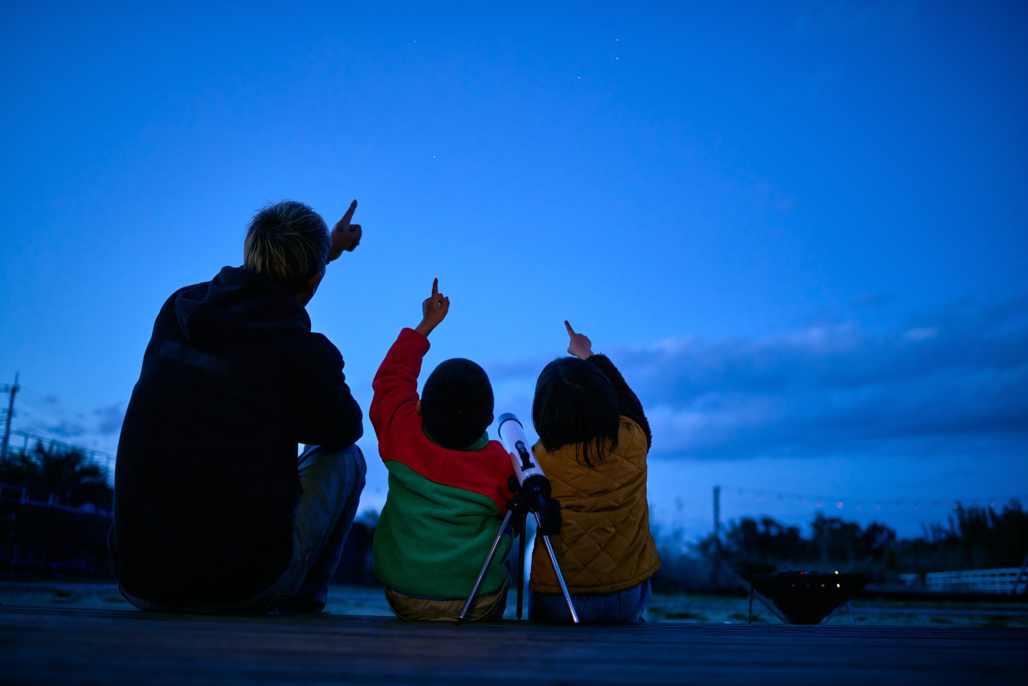 Imagen ilustrativa de un papá con sus dos hijos viendo al cielo, teniendo a su lado un telescopio (Crédito: Getty Images)