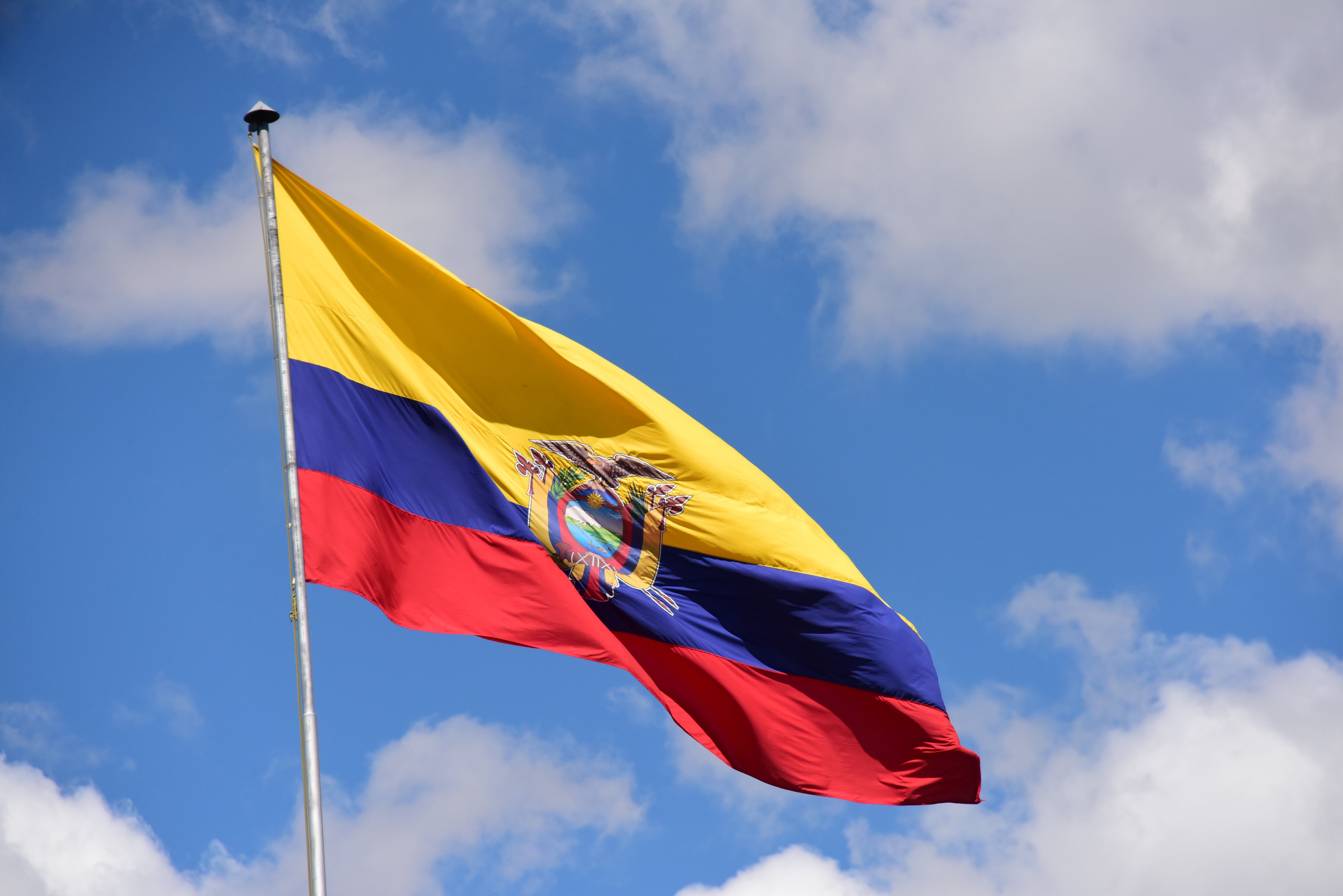 The Ecuadorean flag against a blue sky with fluffy clouds