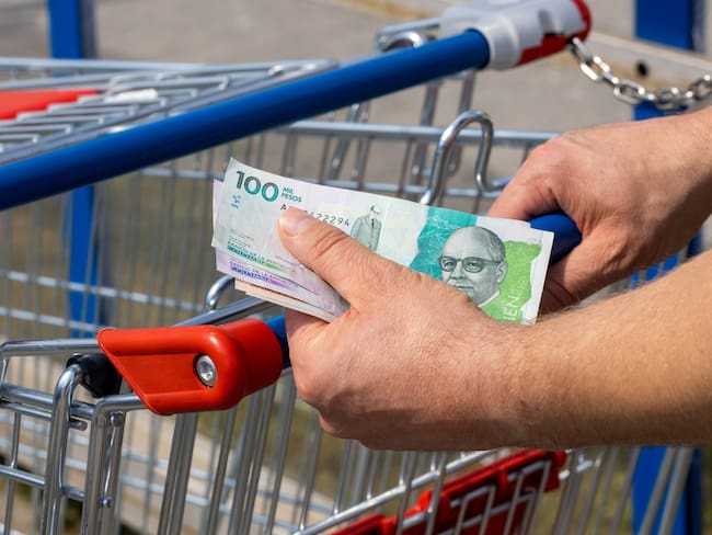 Shopping cart in a supermarket and Colombia pesos, held in hand, Concept of inflation, Rising costs of living, Home budget