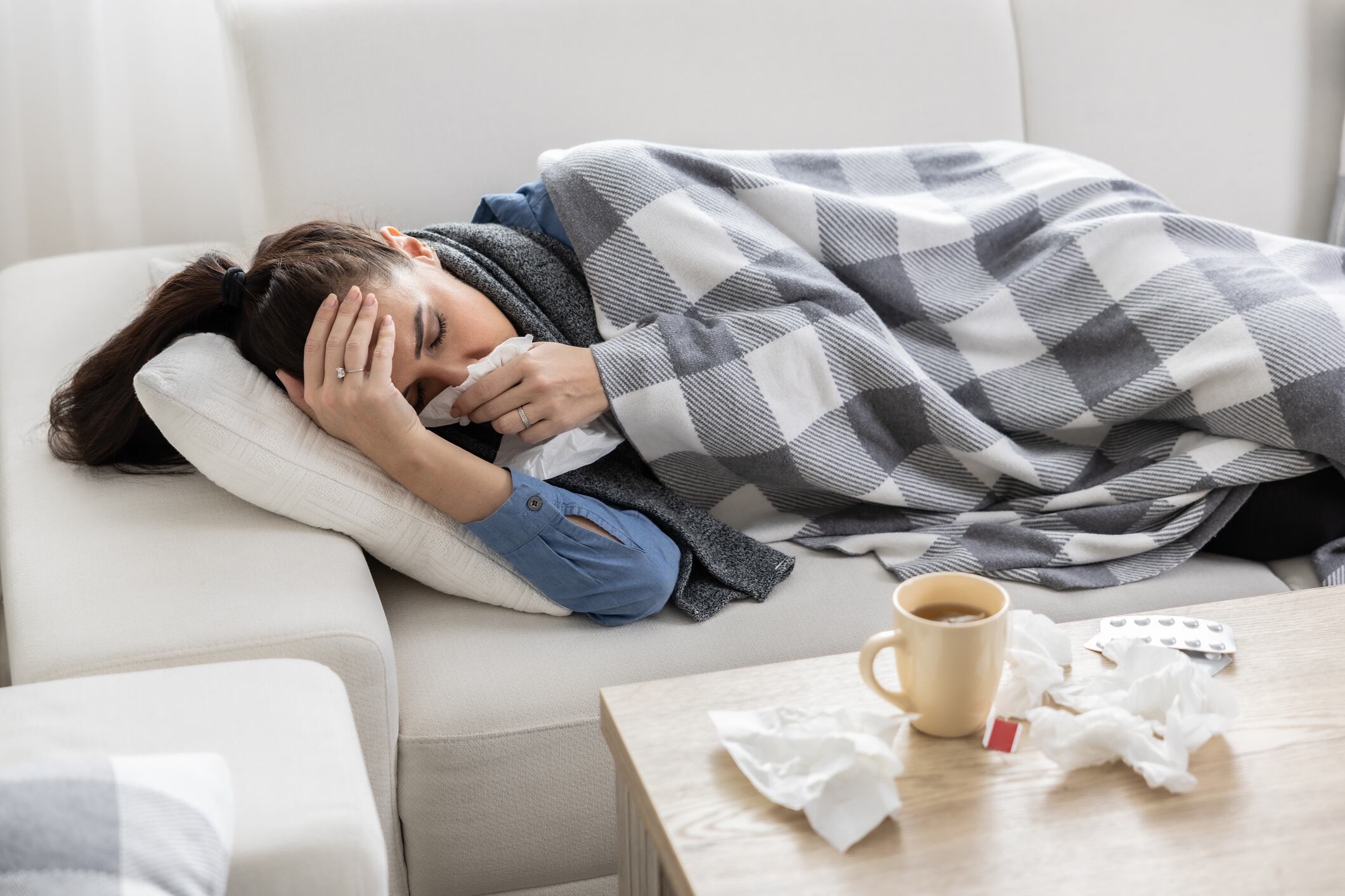 Mujer cubriendo su nariz con un pañuelo junto a una mesa y medicamentos (Foto vía Getty Images)