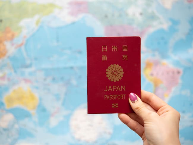 Mujer sosteniendo el pasaporte de Japón, teniendo de fondo un mapa del mundo (Getty Images)