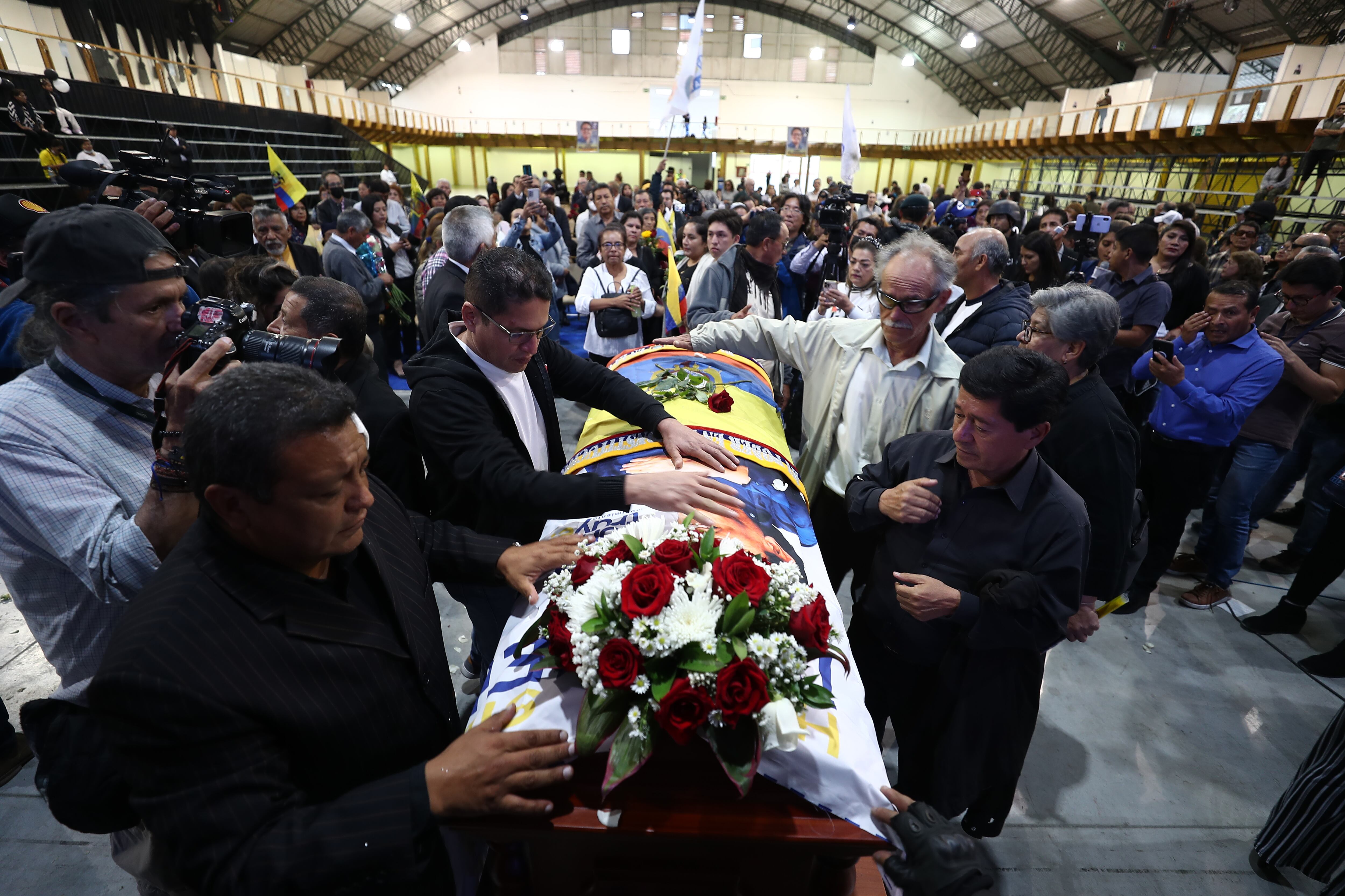 -FOTODELDÍA- AME9921. QUITO (ECUADOR), 11/08/2023.- Varias personas reaccionan junto al féretro del candidato Fernando Villavicencio, durante un velatorio público en un recinto ferial al que fue llevado previo a su entierro, hoy, en Quito (Ecuador). El féretro de Fernando Villavicencio, el candidato a la Presidencia de Ecuador asesinado el miércoles, salió del cementerio al que había sido trasladado para tener un breve velatorio público antes de regresar al camposanto y proceder con su inhumación. Después de haber sido velado de manera íntima y privada por familiares y allegados en un tanatorio de Quito, el féretro con los restos mortales de Villavicencio partió primero al cementerio y, luego de realizar allí una breve ceremonia, salió hacia un recinto ferial donde su círculo cercano había previsto un homenaje póstumo. EFE/ José Jácome