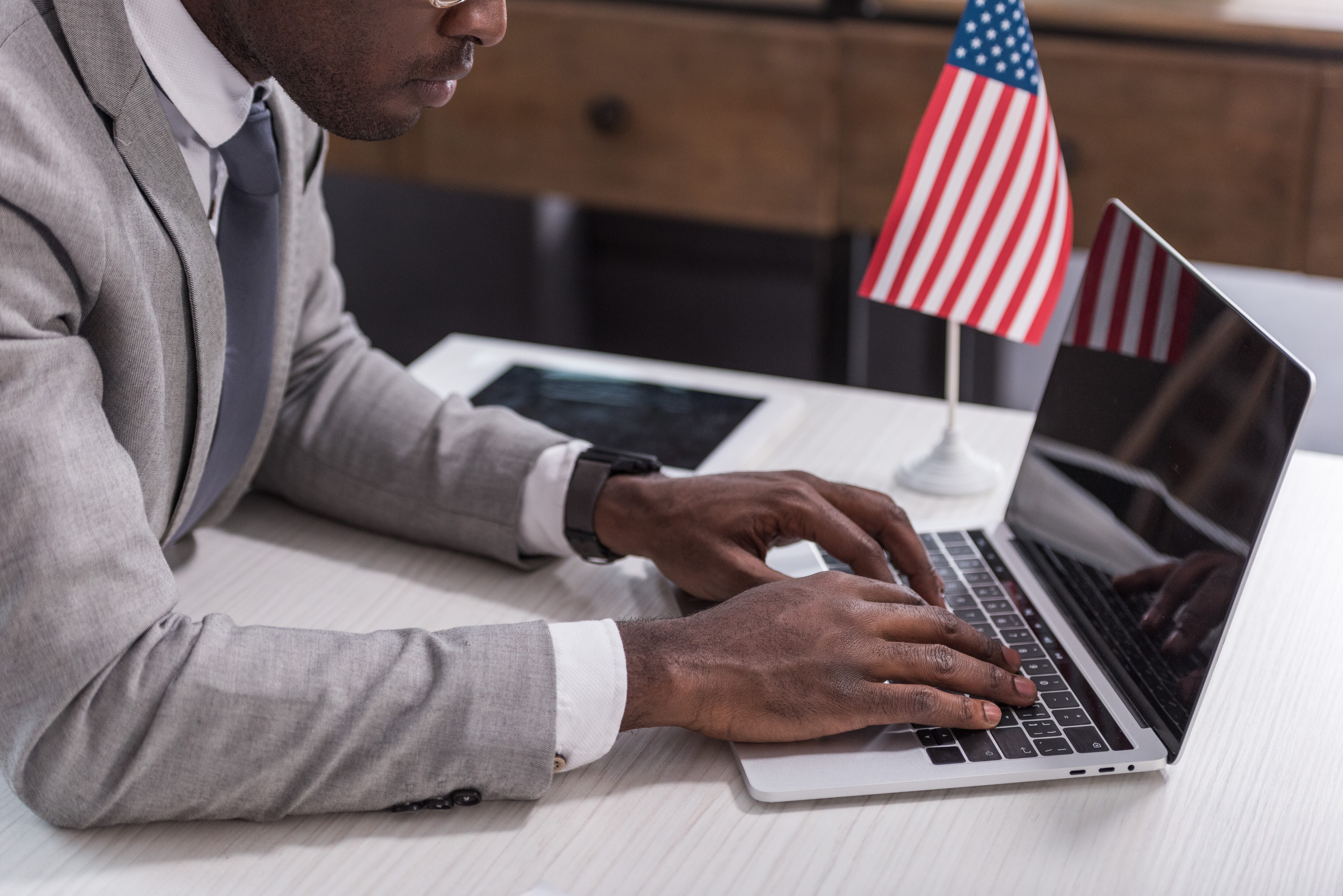 Perona trabajando en el computador con una bandera de Estados Unidos de fondo (Foto vía Getty Images).