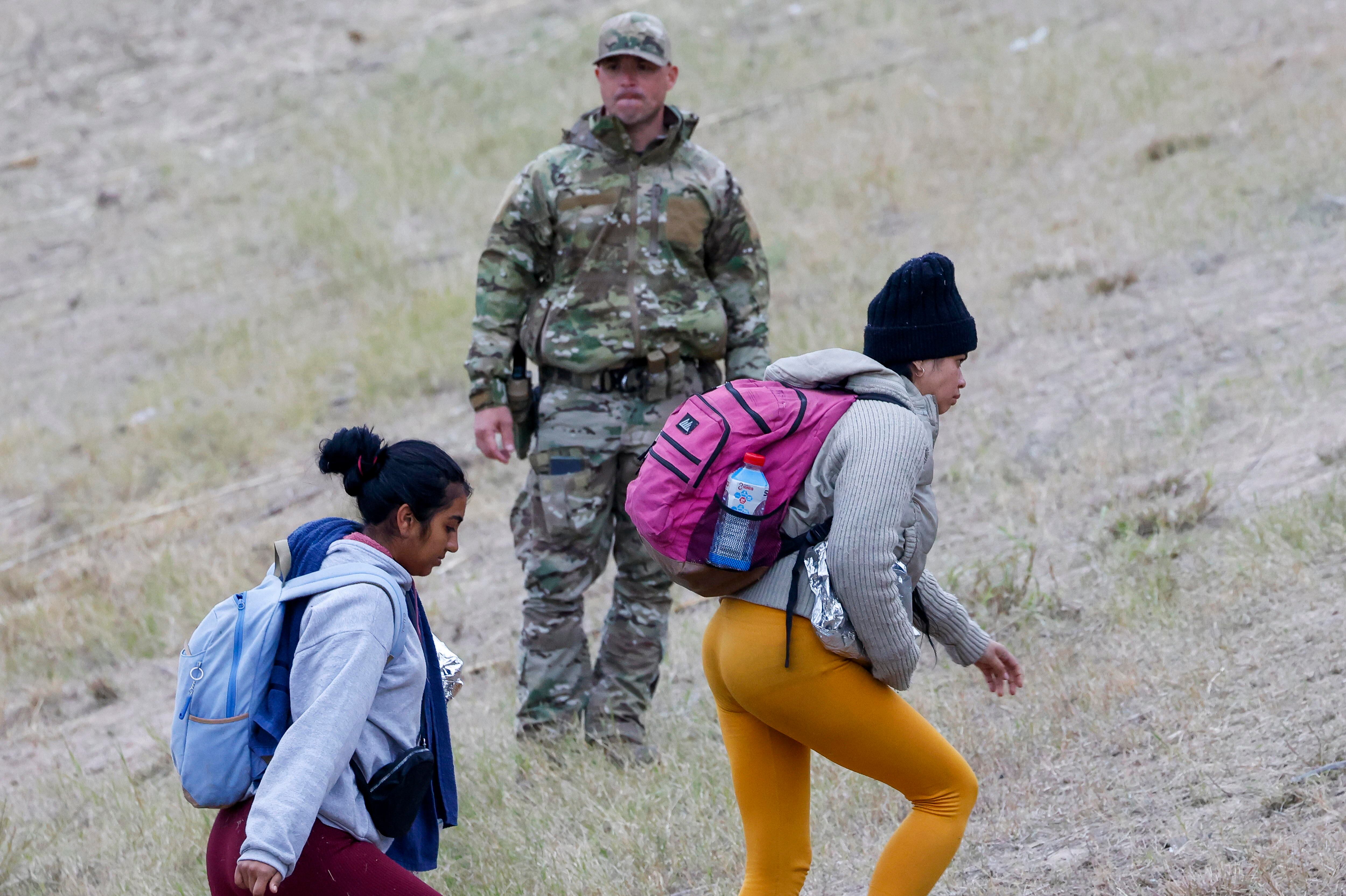 Eagle Pass (United States), 21/12/2023.- A Texas National Guard (C) watches as migrants walks up the hill at Shelby Park in Eagle Pass, Texas, USA, 21 December 2023. It has been reported over the past few days that an average of 12,000 migrants have crossed the border. Texas Governor Greg Abbott has passed a law that if a migrant crosses illegally they can be arrested. EFE/EPA/Adam Davis