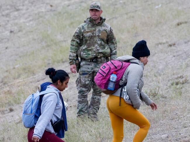Eagle Pass (United States), 21/12/2023.- A Texas National Guard (C) watches as migrants walks up the hill at Shelby Park in Eagle Pass, Texas, USA, 21 December 2023. It has been reported over the past few days that an average of 12,000 migrants have crossed the border. Texas Governor Greg Abbott has passed a law that if a migrant crosses illegally they can be arrested. EFE/EPA/Adam Davis