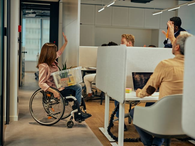 Mujer con situación de discapacidad despidiéndose de sus compañeros de trabajo (Getty Images)