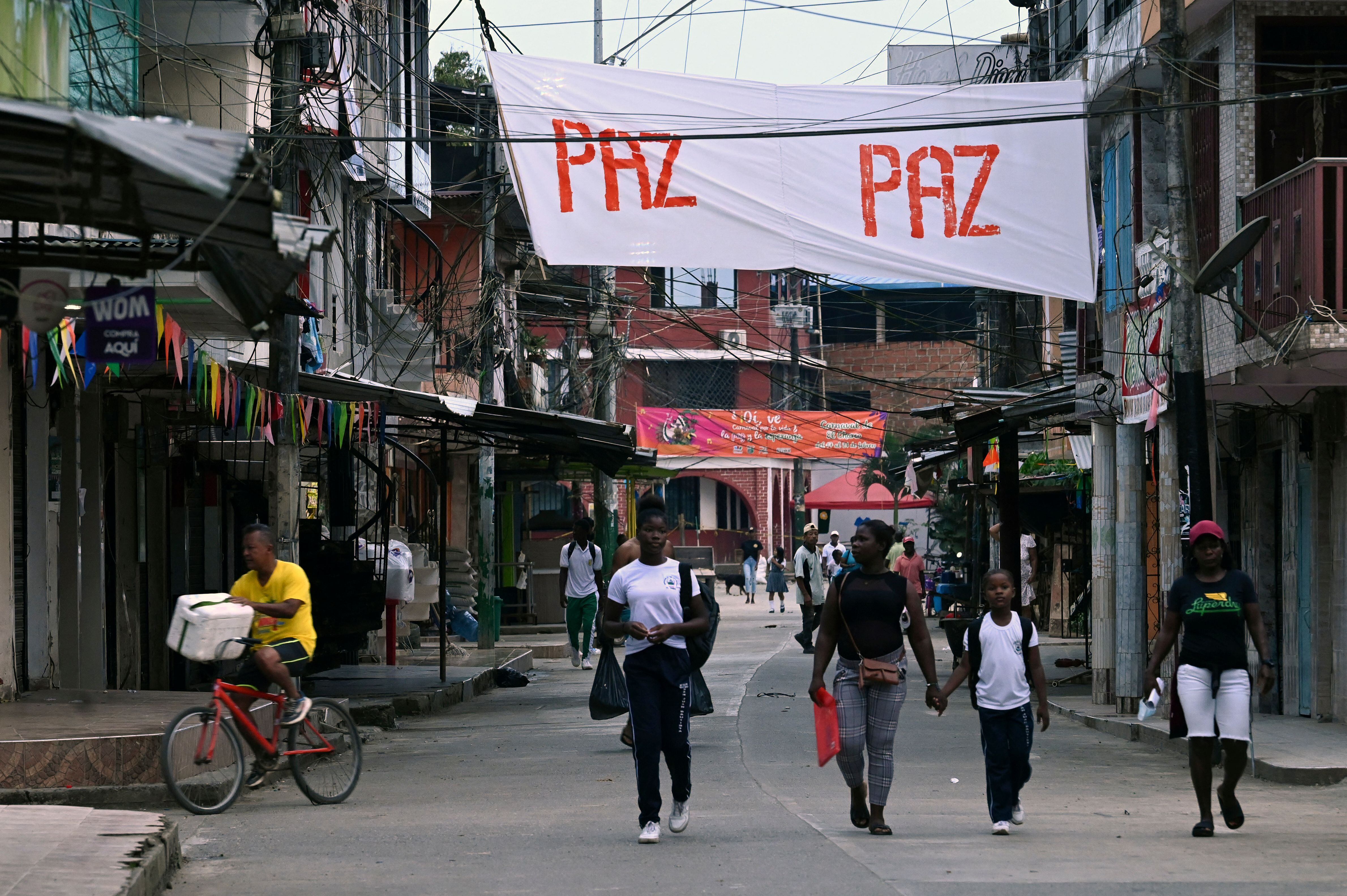 People walk by a banner reading "Peace" in the town of El Charco, in the municipality of the same name in the Colombian department of Narino, on March 3, 2023. - In the humid Colombian jungle and under plastic tents, a rebel commando shelters, on the verge of talking with an ex-guerrilla who "inspires confidence" in them. Dissidents of the extinct FARC await the start of new peace negotiations, this time with leftist President Gustavo Petro. (Photo by Joaquín SARMIENTO / AFP) (Photo by JOAQUIN SARMIENTO/AFP via Getty Images)