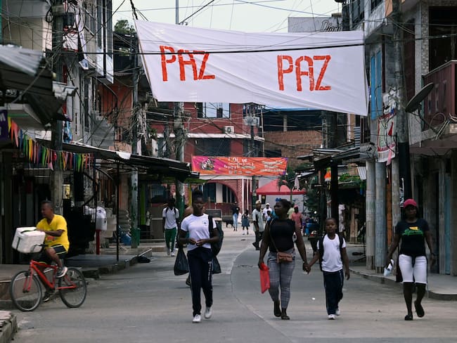 People walk by a banner reading "Peace" in the town of El Charco, in the municipality of the same name in the Colombian department of Narino, on March 3, 2023. - In the humid Colombian jungle and under plastic tents, a rebel commando shelters, on the verge of talking with an ex-guerrilla who "inspires confidence" in them. Dissidents of the extinct FARC await the start of new peace negotiations, this time with leftist President Gustavo Petro. (Photo by Joaquín SARMIENTO / AFP) (Photo by JOAQUIN SARMIENTO/AFP via Getty Images)